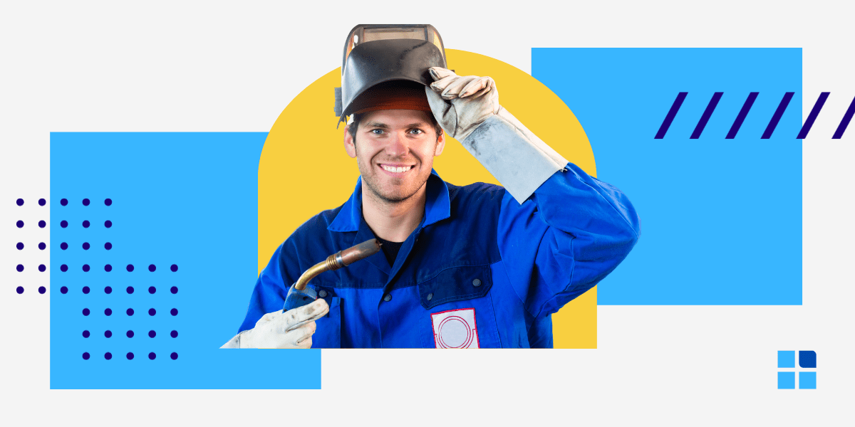Smiling welder in blue overalls lifts helmet, holding torch.