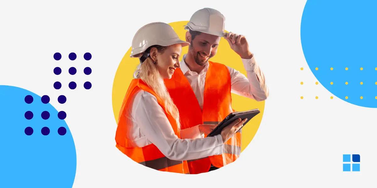 Two construction workers in hard hats and orange vests smile as they review a tablet.