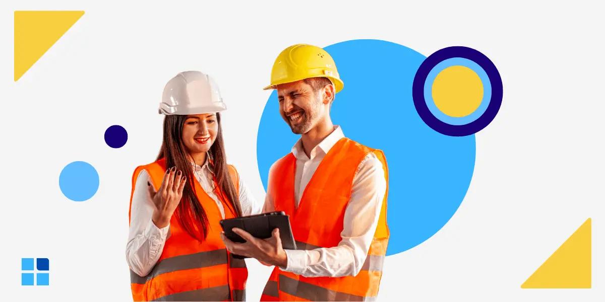 Two construction workers, a woman and a man, in helmets and orange vests, happily discuss a tablet.