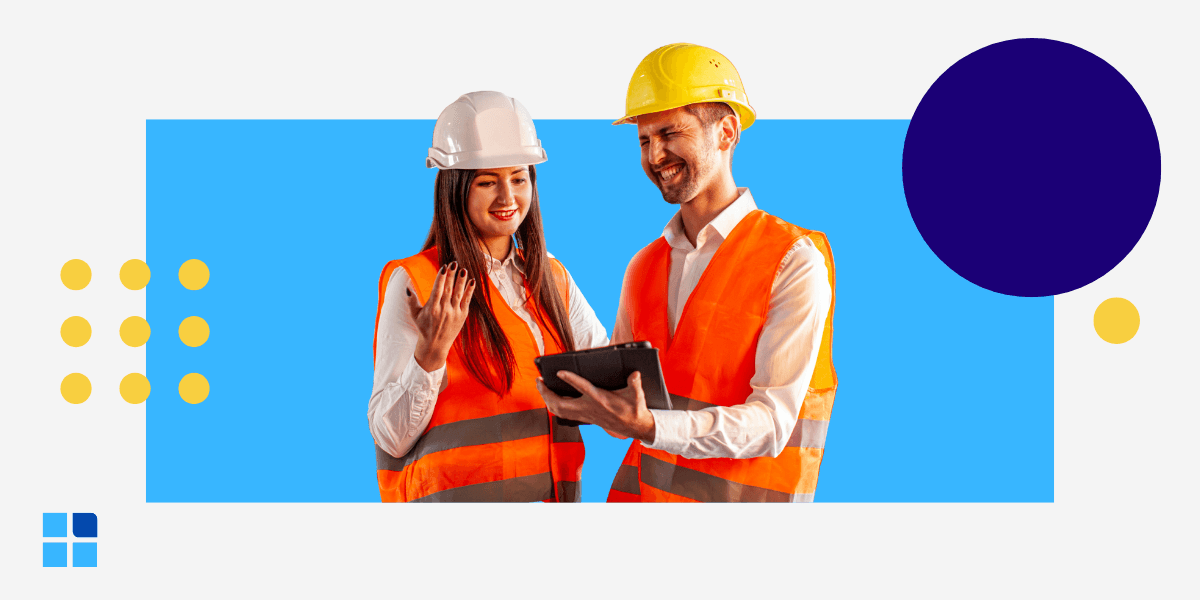 Two managers in hard hats and safety vests smiling while using a tablet.