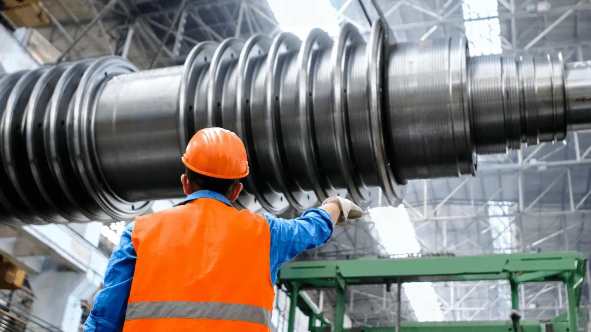 An industrial engineer inspects a massive turbine rotor in a heavy manufacturing facility.