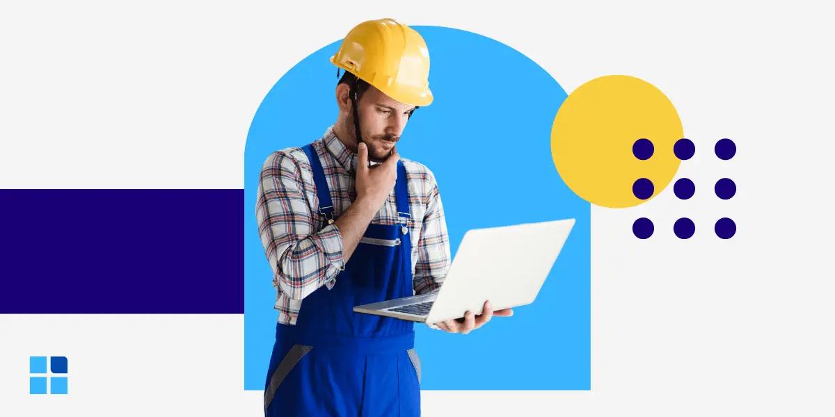 A construction worker in a yellow hard hat and blue overalls holds a laptop, looking thoughtful.
