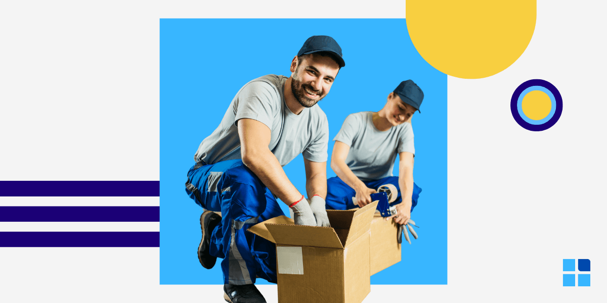 Two workers in blue uniforms and caps are packing a cardboard box, smiling.