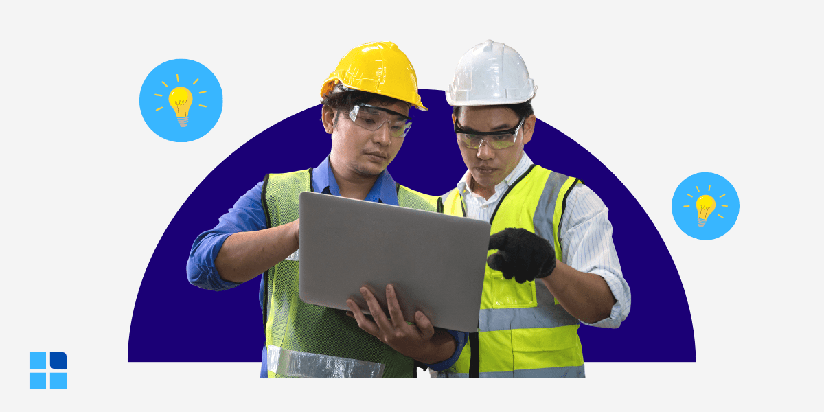 Two construction workers wearing hard hats and safety vests examine a laptop, appearing focused.