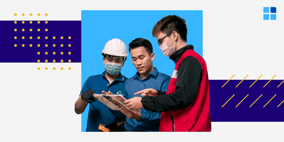Three men, one in a hard hat, discuss a document. Two wear masks.