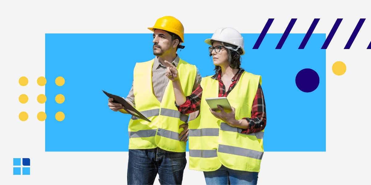 Two construction workers wearing hard hats and reflective vests hold tablets, discussing plans.