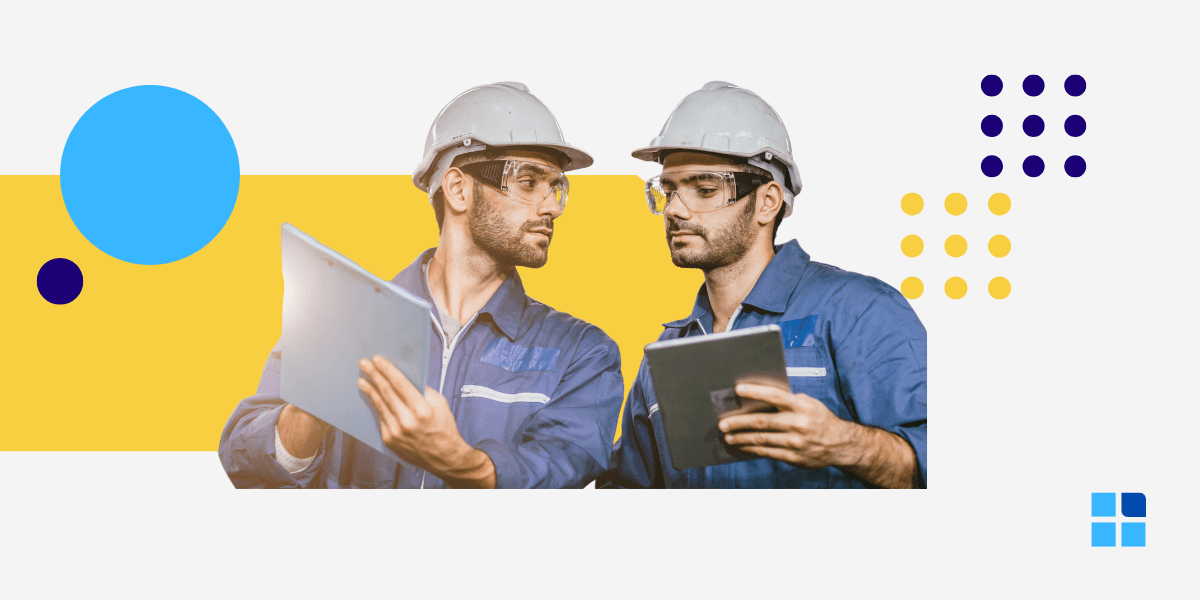 Two engineers in blue uniforms and helmets discuss plans.