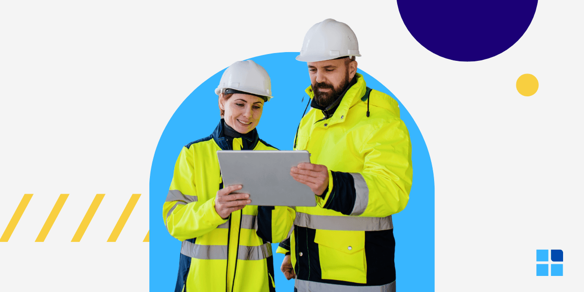 Two construction workers in high-visibility jackets and hard hats are reviewing a tablet together.