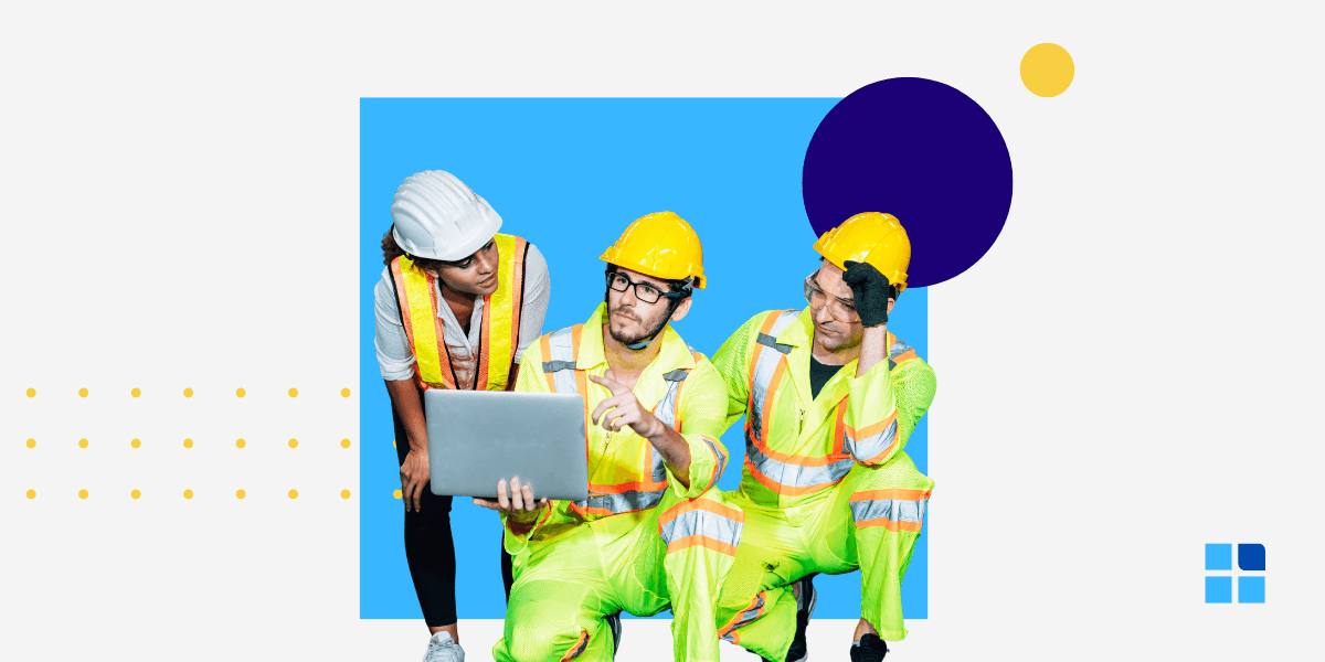 Three construction workers in reflective gear and helmets gather around a laptop.