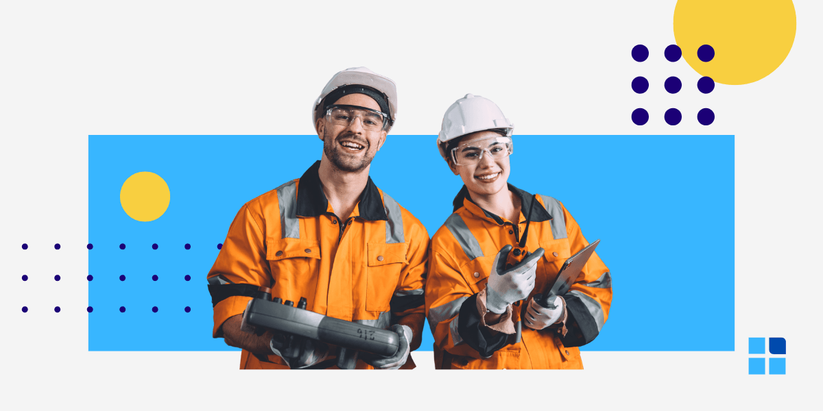 Two smiling construction workers in orange safety jackets and helmets hold tools.